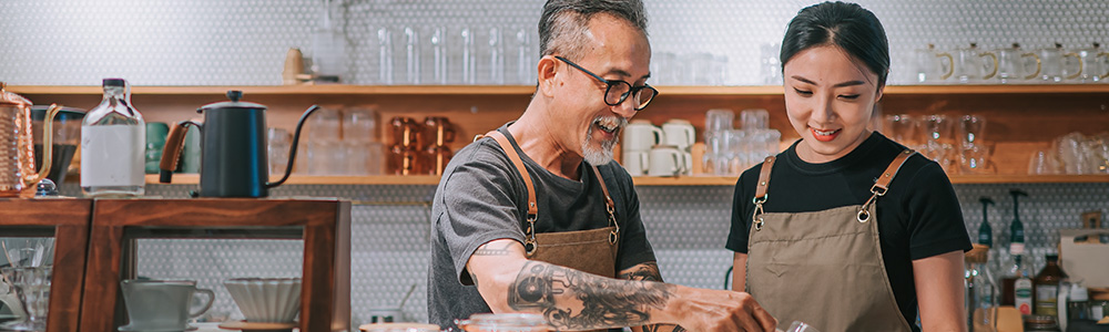 A tattooed barista teaches another barista