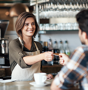 A business owner greeting a customer and taking their credit card for a purchase.