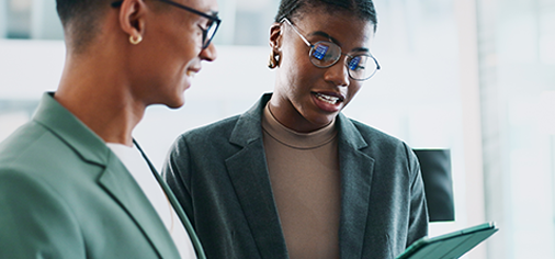 A woman with short hair and glasses shows her table to a colleague