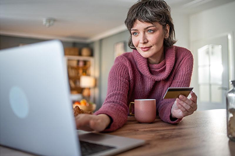 A woman with her coffee, types at her laptop while holding her credit card