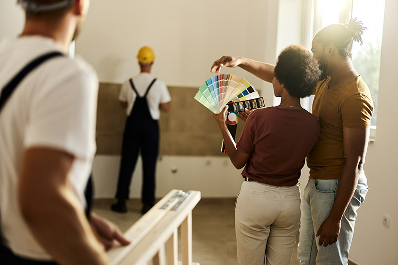 A couple looks at paint swatches as a construction teams works on their remodel
