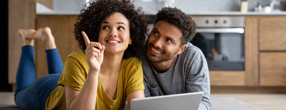 A happy couple lay on the floor of their kitchen with a laptop