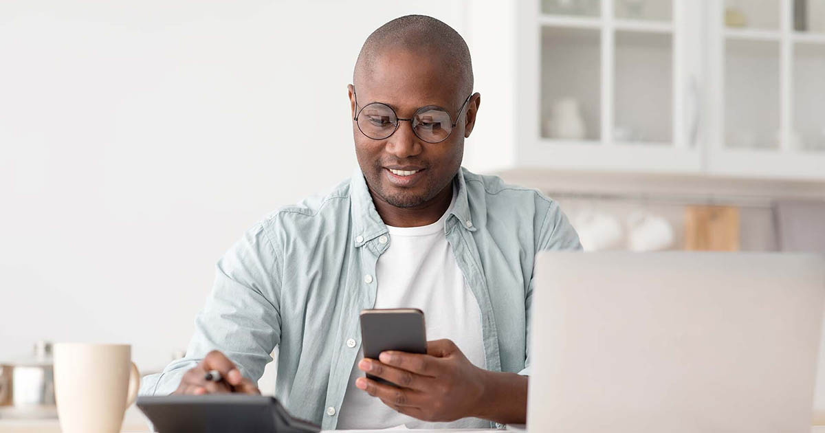 Savings and finances concept. Mature black man using calculator, phone and laptop computer