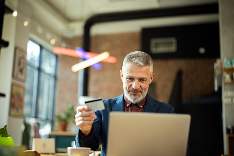 An older man looks at his card while looking at his laptop
